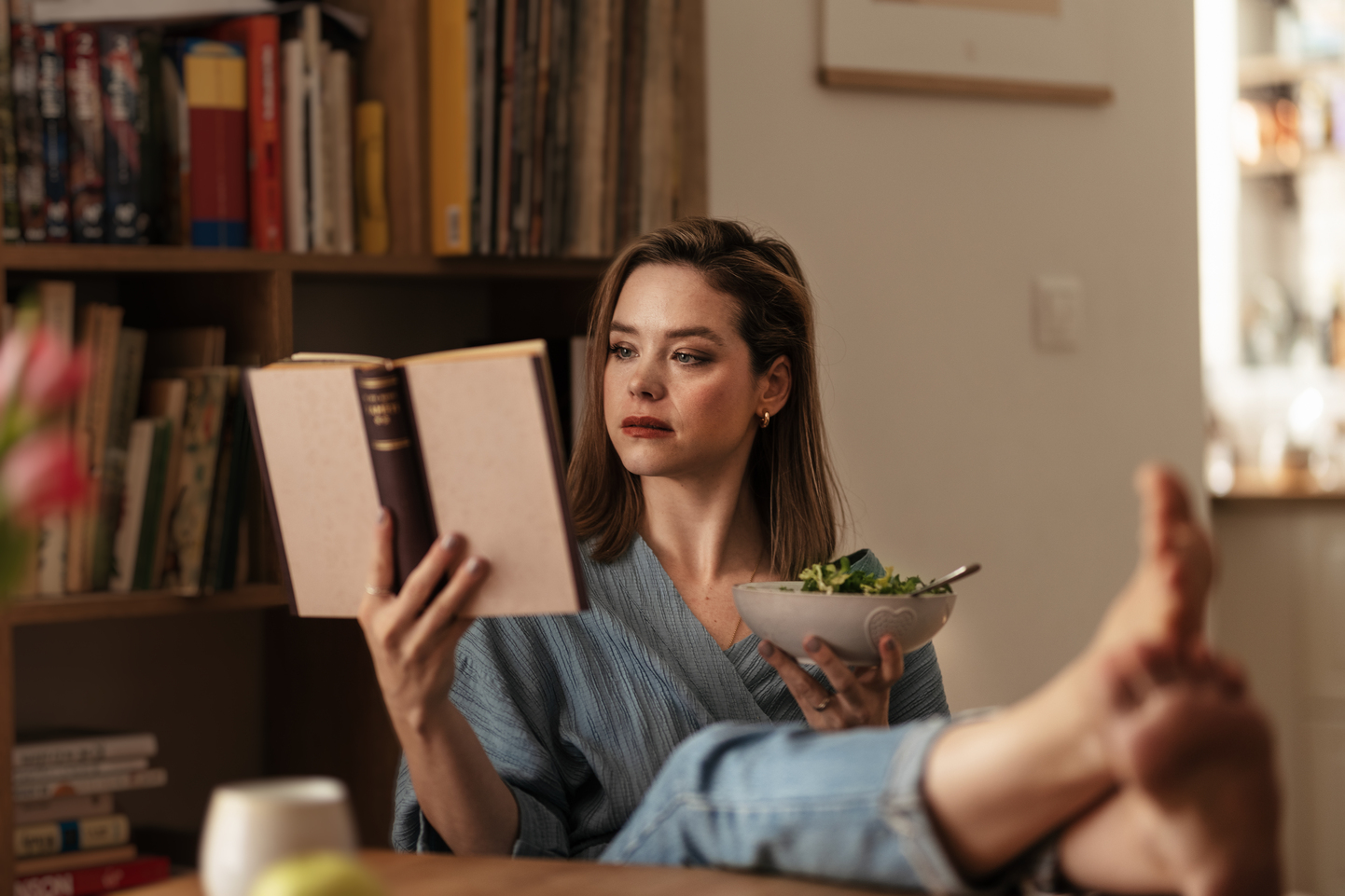 Woman resting at home, reading book and eating salad.